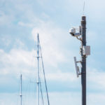 CCTV security cameras on pole in cloudscape and yacht masts backdrop in seaport